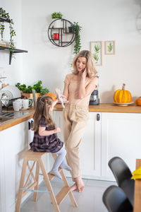 Full length of mother talking on phone in kitchen