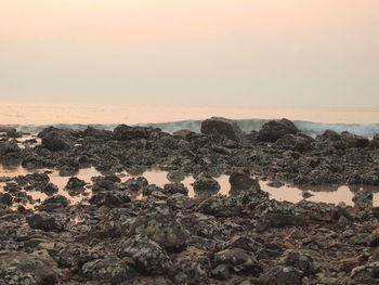 Rocks on shore against sky during sunset