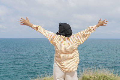 Rear view of woman standing at beach against sky