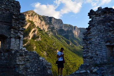 Man using phone amidst stone wall against mountain