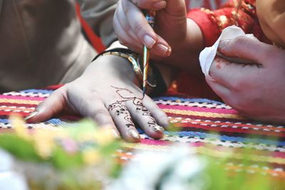 Midsection of woman applying henna tattoo on friend hand