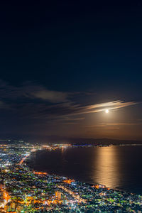 High angle view of illuminated city by sea against sky at night