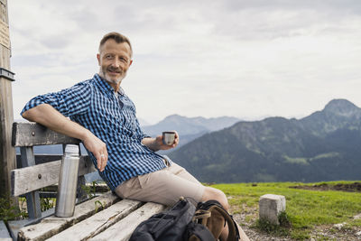 Man holding coffee while sitting on bench