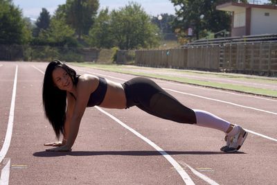 Full length of young woman exercising on running track