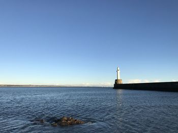 Lighthouse by sea against clear sky