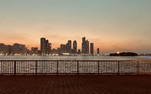 Illuminated buildings by sea against sky during sunset