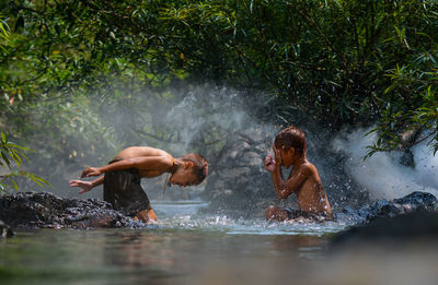 Side view of shirtless brothers bathing in river at forest