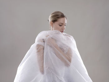 Portrait of woman wrapped in plastic against gray background