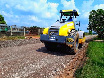 Yellow cart on road amidst field against sky