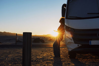 Rear view of woman standing against sky during sunset