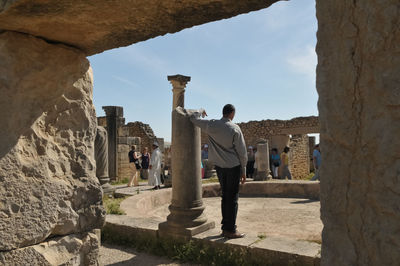 Rear view of man standing at old ruins against sky