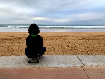 Rear view of girl sitting on skateboard at beach