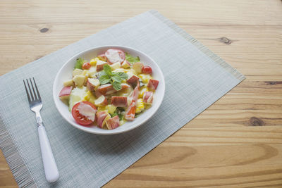 Mixed vegetable and fruit salad with crab sticks on a white plate, ready to serve