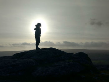 Silhouette man standing on rock against sky during sunset