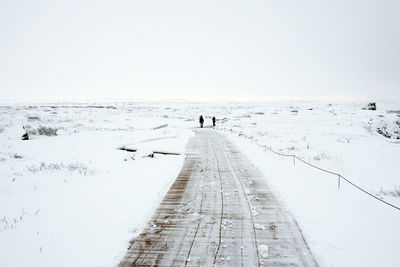 Footpath amidst snow covered field against sky