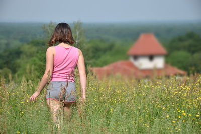 Rear view of teenage girl standing on field against sky
