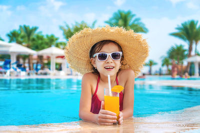 Portrait of smiling girl with orange glass at poolside