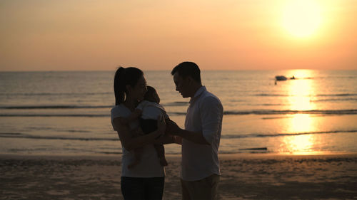 Men standing on beach against sky during sunset