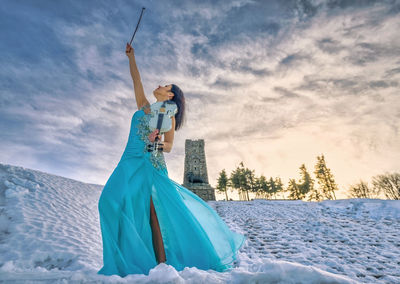 Woman standing with violin against sky during winter