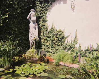 Statue of woman standing by plants against trees