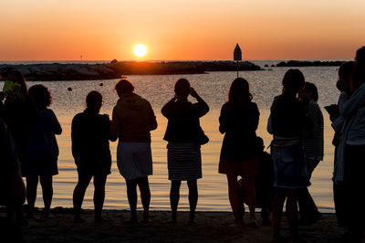 Silhouette people standing at beach during sunset