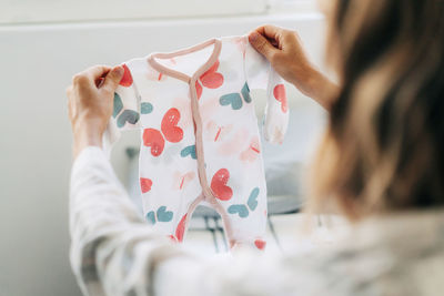 An unrecognizable pregnant woman holds in her hand and looks at an infant bodysuit.