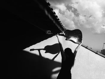 Low angle view of silhouette man holding umbrella against sky