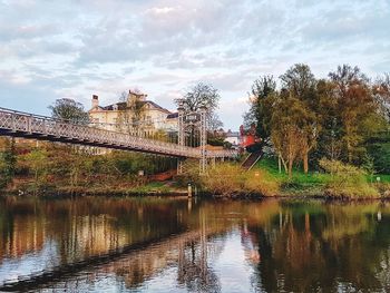 Bridge over river by buildings against sky