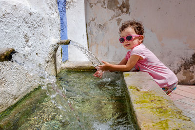Portrait of girl wearing sunglasses cleaning hands in water outdoors