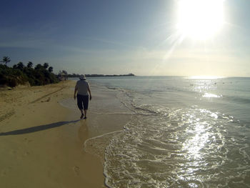 Rear view of man fishing on beach against sky