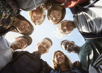 Low angle portrait of smiling friends huddling at university campus against sky