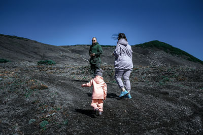 Rear view of friends walking on mountain against blue sky