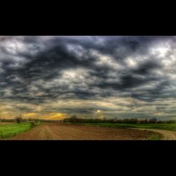 Road passing through field against cloudy sky