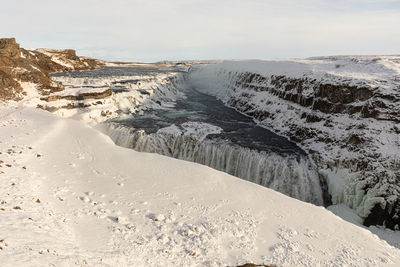 Scenic view of snow covered land and waterfall against sky