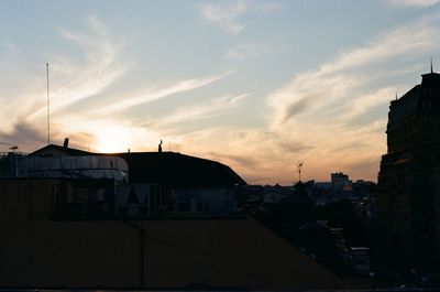 Silhouette buildings against cloudy sky at sunset