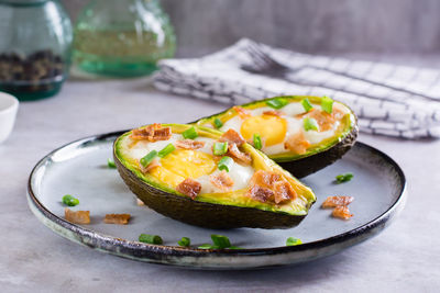 Baked avocado with egg, bacon and chives on a plate on the table for a keto diet