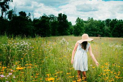 Rear view of woman with arms raised on field against sky