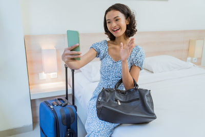 Portrait of young woman using mobile phone while sitting on bed at home