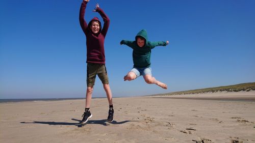 Full length of friends jumping on beach against clear sky