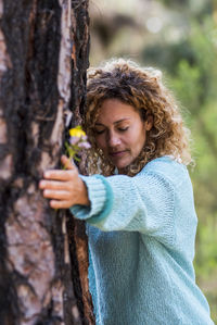 Young woman standing by tree trunk