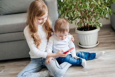 Girl with a baby brother sitting on the floor with a smartphone