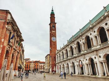 People in front of historic building against sky in city