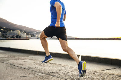 Low section of man running against sea during sunset