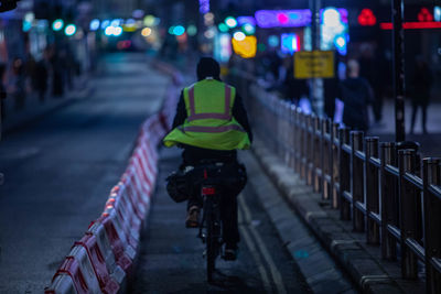 Rear view of man riding bicycle on street at night