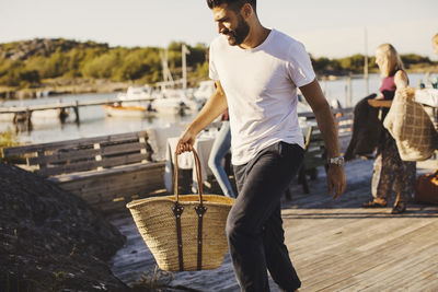 Man carrying picnic basket while walking on jetty during sunny day