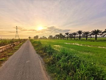 Road amidst field against sky during sunset