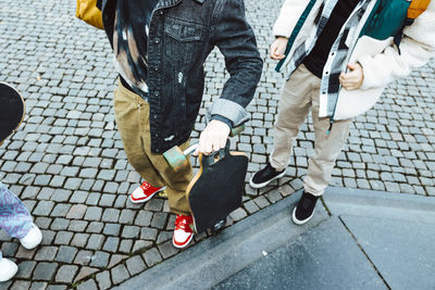 Low section of boy with skateboard standing by male friend on footpath