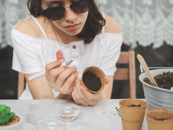 Caucasian teenage girl in sunglasses and gardening gloves signs a glass with a cardboard marker.