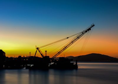 Silhouette crane at commercial dock against clear sky