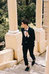 A beautiful young man, the groom in an elegant wedding suit, stands posing in the city's old park